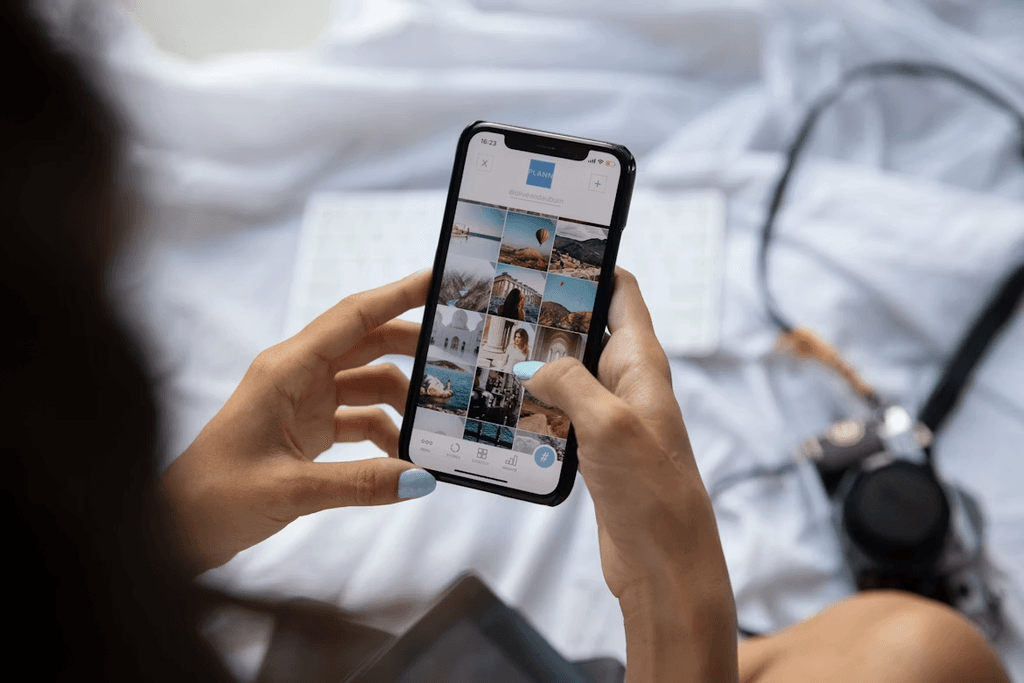 Woman scrolling on social media on her phone while sat on bed, with a film camera in the background