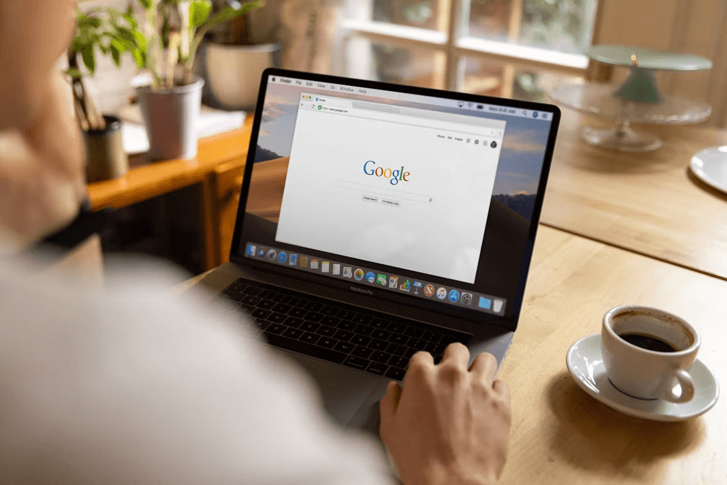 Person sat at their desk on a laptop searching on Google while drinking a cup of coffee